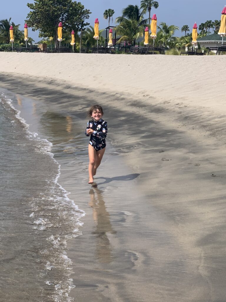 A young girl running in the sand, holding a shell.