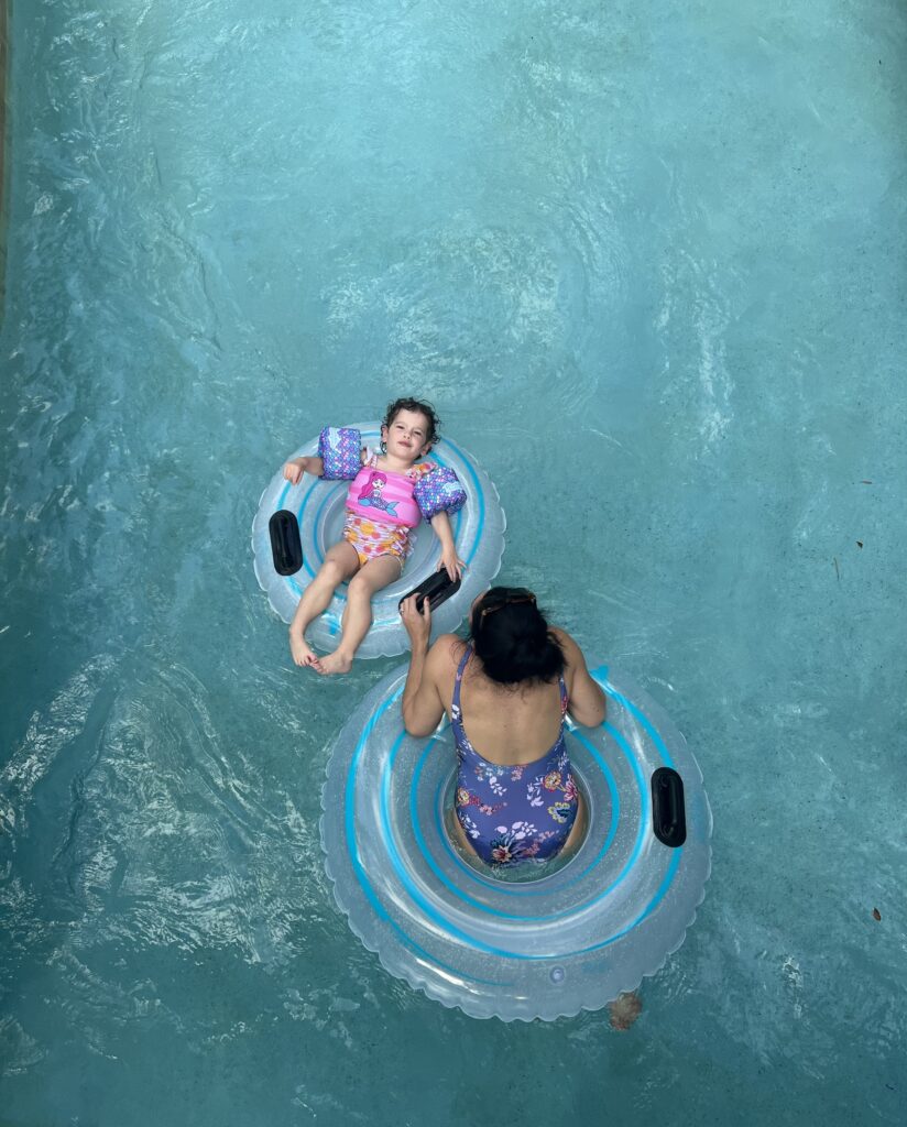 A woman and a child floating in bright blue water still water. The child is smiling at the camera and wearing a hot pink and purple swimsuit. 