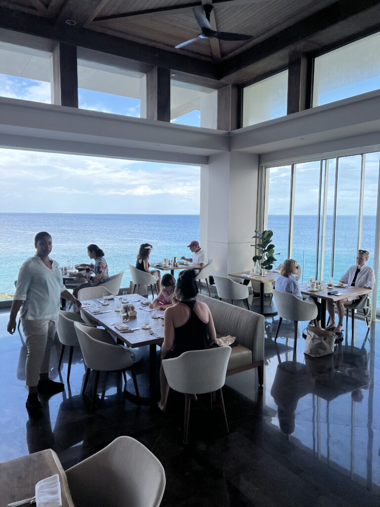 Four Seasons Anguilla features Salt, where breakfast is served to families daily. A family sits down at a large table overlooking the ocean. 