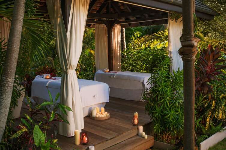 Two massage tables outdoors surrounded by greenery. 