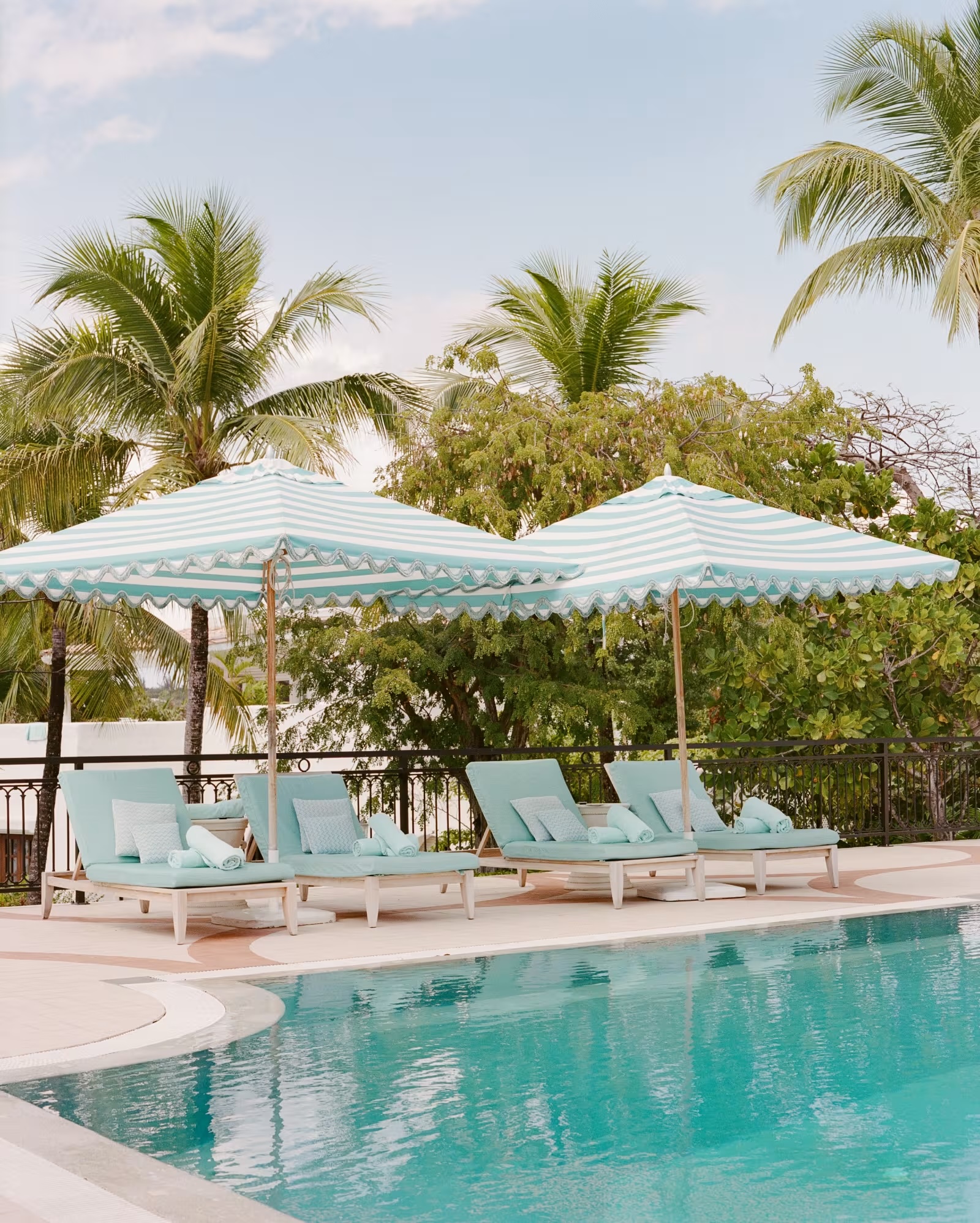 Blue and white lounge chairs located along a poolside with green foliage in the background.